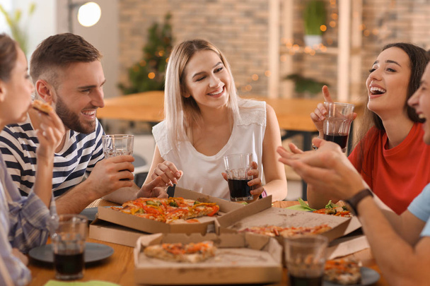 Nuoret syövät pizzaa pöydässä
 - Valokuva, kuva