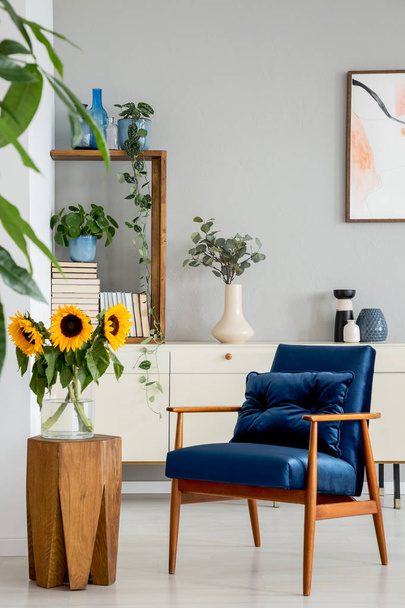 Sunflowers on wooden stool next to blue armchair in living room interior with poster. Real photo - Foto, afbeelding