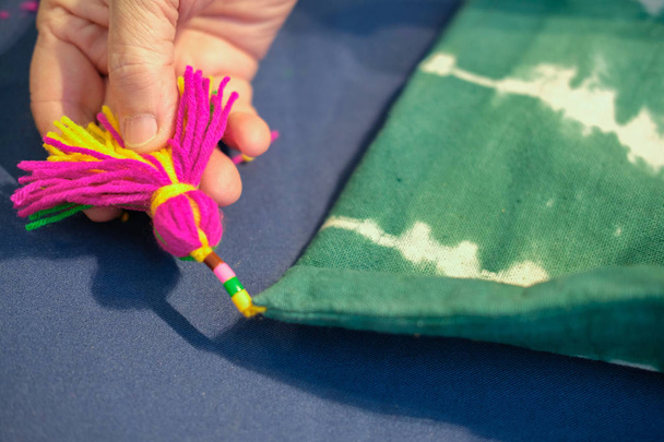 hand holding kntting tassel decorating on handmade tie dye fabric handbag - Photo, Image