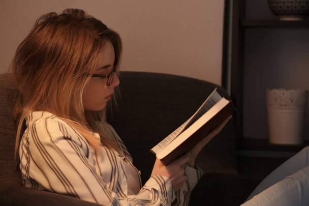 Young woman reading book at home in evening - Foto, Imagen