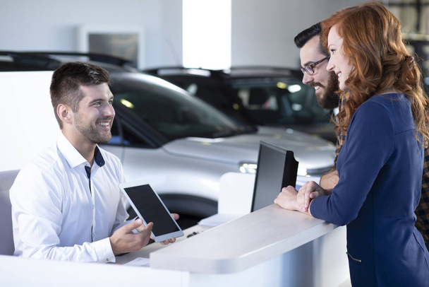 Smiling professional car dealer showing an offer to happy buyers on a tablet - 写真・画像