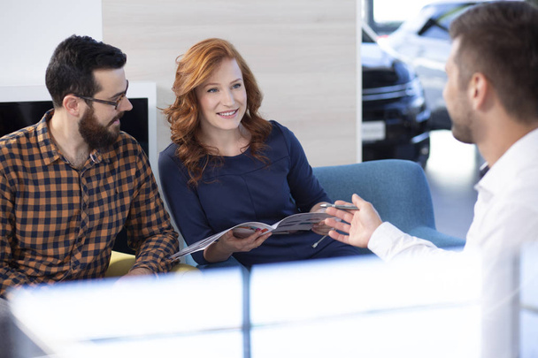 Couple looking at car offer and talking to a dealer in a car showroom - Foto, Imagem