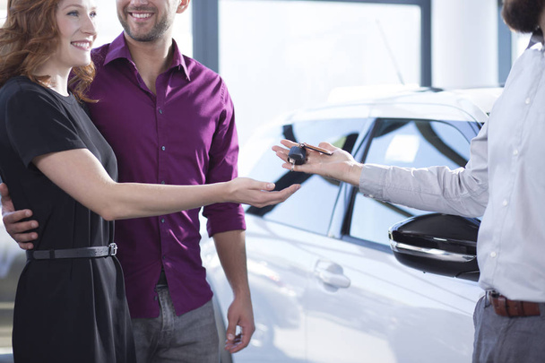 Car dealer giving keys to happy woman and smiling man in a dealing salon - Fotoğraf, Görsel