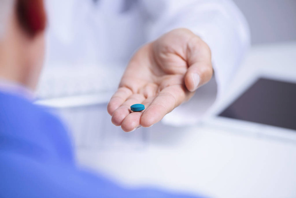 closeup of a caucasian doctor man, in a white coat, giving a blue pill to a senior caucasian patient man, sitting both at a doctors desk - Photo, Image