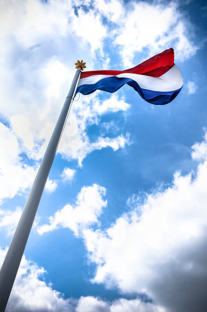 Nederlandse vlag zwaaien op Koninklijke vlaggenmast met gouden kroon in top. Zonnige scène met Nederlandse trots voor nationale of feestelijke gelegenheden - Foto, afbeelding