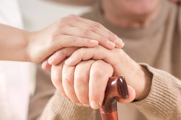 Nahaufnahme von Seniorin Hand in Hand mit Gehstock und hilfsbereiter Betreuerin - Foto, Bild