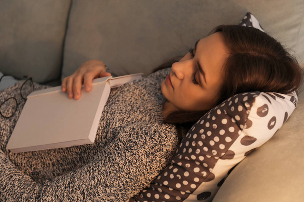 Втомлена молода жінка з книгою спить на дивані вдома
 - Фото, зображення