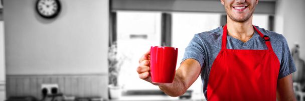 Male waiter holding coffee mug against view of kitchen - Photo, image