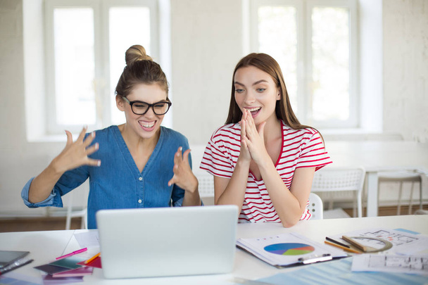 Jóvenes mujeres emocionadas trabajando emocionalmente junto con el ordenador portátil pasar tiempo en la oficina moderna
  - Foto, Imagen