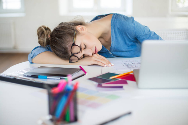 Młody zmęczony kobieta z okulary na głowie spanie na biurko z laptopa w pobliżu spędzanie czasu w nowoczesnym biurze - Zdjęcie, obraz