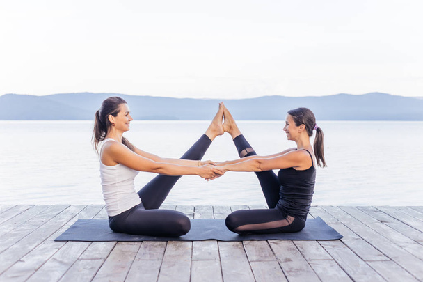 Young attractive smiling women practicing yoga on a lake - Foto, Imagen