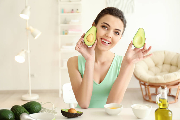 Young woman making nourishing mask with avocado in kitchen - Foto, imagen