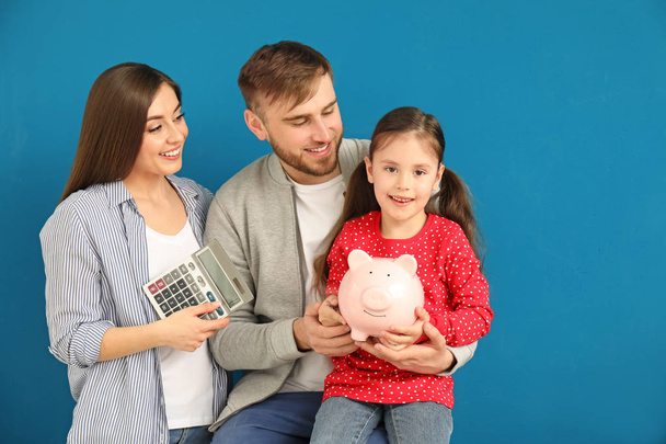 Счастливая молодая семья с банком свиньи и калькулятором на цветном фоне
 - Фото, изображение