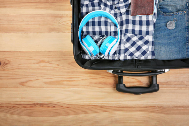 Open suitcase with clothes and tourist's stuff on wooden background - 写真・画像
