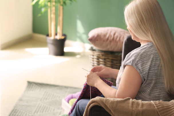 Mature woman sitting on sofa and knitting warm sweater indoors - Photo, Image