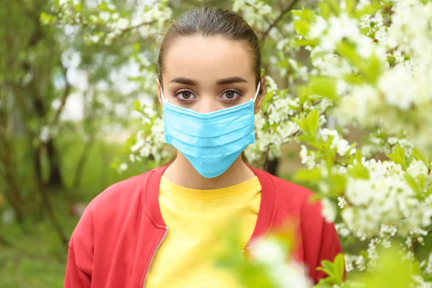 開花木の近くの防護マスクで若い女性。アレルギーの概念 - 写真・画像