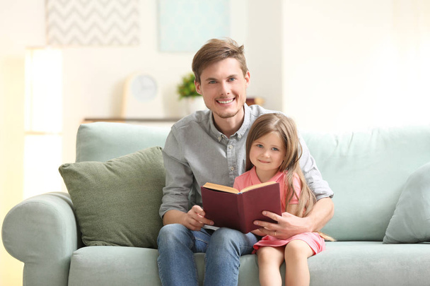 Father and his daughter reading book together at home - Фото, изображение