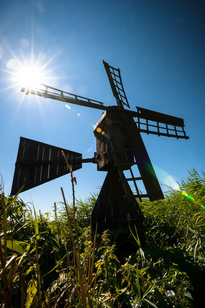Tyypillinen musta tervamainen tuulimylly nurmen ja vesiväylien reunalla olevien vihreiden ruokojen välissä. Ainutlaatuinen hollantilainen maisemakuva, jossa on kulttuuriperintö Alankomaiden maisemassa aurinkoisena päivänä mustuneen taivaan alla, jossa on taustavalo
 - Valokuva, kuva
