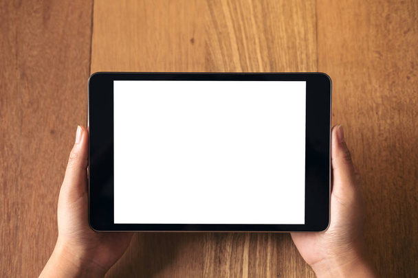 Image maquette des mains tenant et montrant un ordinateur tablette noire avec écran blanc vierge sur une table en bois vintage
  - Photo, image
