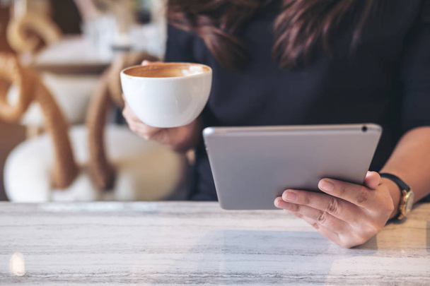 Image rapprochée d'une femme tenant et utilisant un ordinateur tablette tout en buvant du café dans un café moderne
 - Photo, image