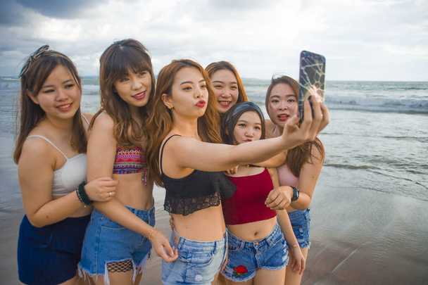 lifestyle beach portrait of Asian Korean and Chinese women, group of happy beautiful young girlfriends taking selfie picture together with mobile phone smiling cheerful enjoying girls holidays trip - Photo, Image