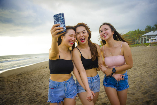 lifestyle beach portrait of Asian Korean and Chinese women, group of happy beautiful young girlfriends taking selfie picture together with mobile phone smiling cheerful enjoying girls holidays trip - Photo, Image