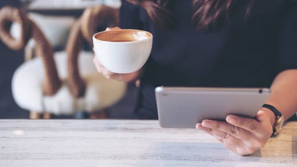 Immagine in primo piano di una donna che tiene e utilizza tablet pc mentre beve caffè in caffè moderno
 - Foto, immagini