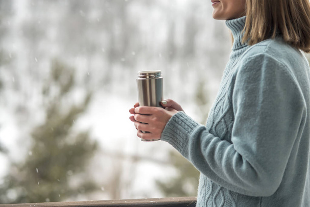 Woman in the background of a winter forest in a thermos bottle in hands - Foto, imagen