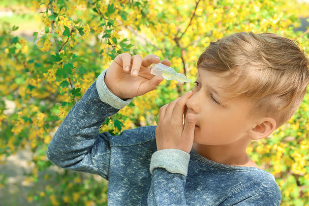 Μικρό αγόρι χρησιμοποιώντας μάτι σταγόνες κοντά ανθίζοντας δέντρο. Αλλεργία έννοια - Φωτογραφία, εικόνα