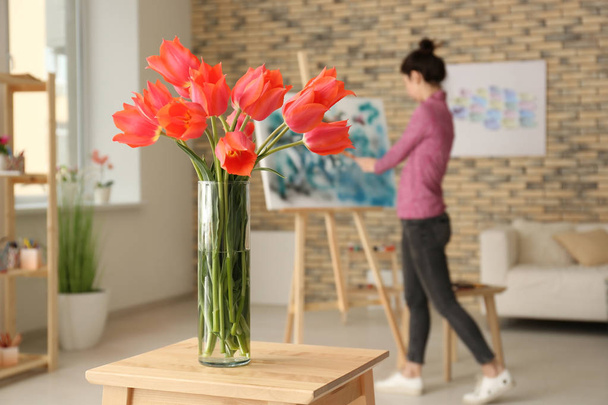 Wazon z piękne tulipany i niewyraźne kobieta malarstwo w pomieszczeniu - Zdjęcie, obraz