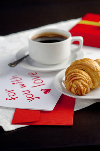 Kuppi kahvia croissantin kanssa. Juhlallinen aamiainen ystävänpäivälle rakkausviestillä
. - Valokuva, kuva
