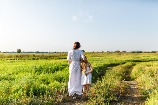 rear view of mother and daughter standing on path in green meadow - Fotó, kép