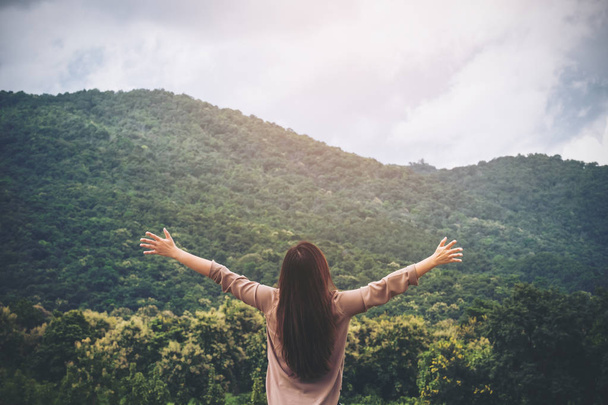 Una mujer se volvió y estiró los brazos con cielo azul, naturaleza verde y fondo de montaña
 - Foto, Imagen