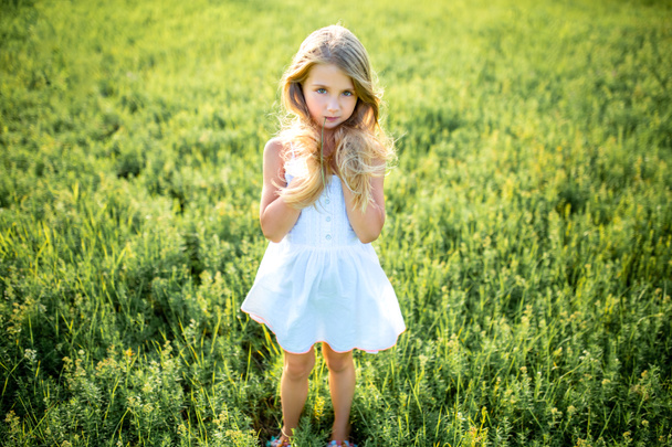 милый маленький ребенок в белом платье позирует в зеленом поле и смотрит в камеру
 - Фото, изображение