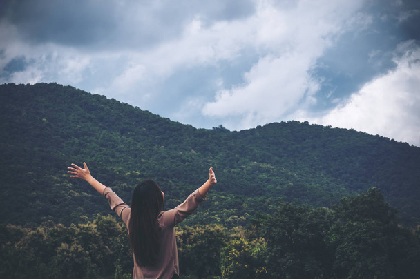 Μια γυναίκα να γυρίσει πίσω και να τεντώνεται τα όπλα με το μπλε του ουρανού, το πράσινο της φύσης και το υπόβαθρο βουνό - Φωτογραφία, εικόνα