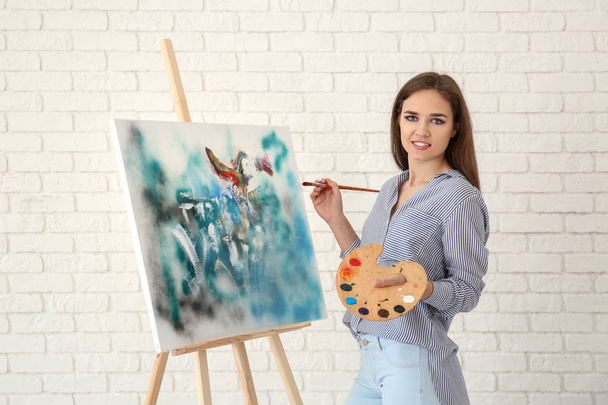 Giovane artista femminile con cavalletto disegno contro muro di mattoni bianchi
 - Foto, immagini