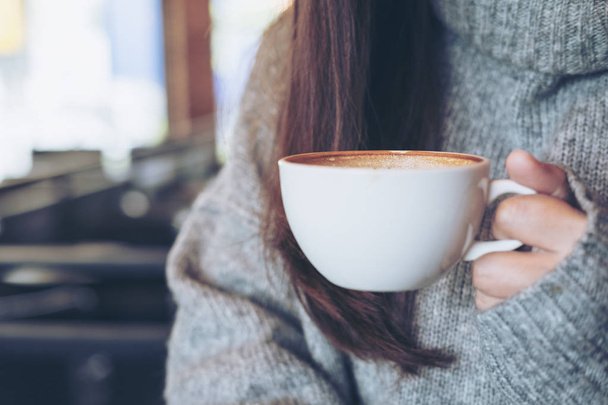 Крупный план изображения женщины, держащей в руках чашку горячего кофе, сидящей в кафе зимой
 - Фото, изображение