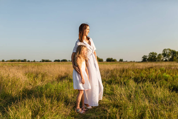mother and daughter standing in field and looking at sunset - 写真・画像