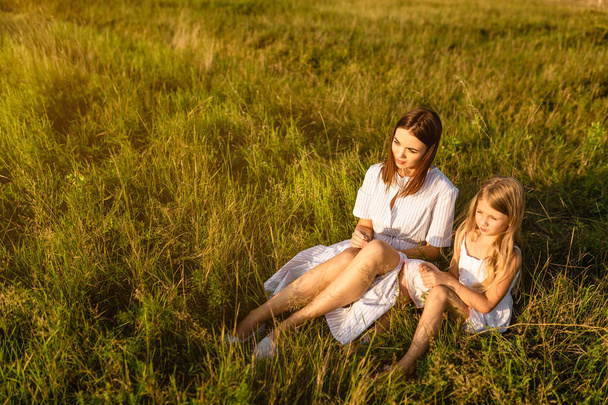 matka i córka siedzi na zielonej trawie i patrząc na zachód słońca - Zdjęcie, obraz