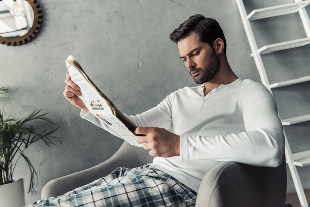Beau homme en vêtements décontractés lit un journal tout en se reposant à la maison
 - Photo, image