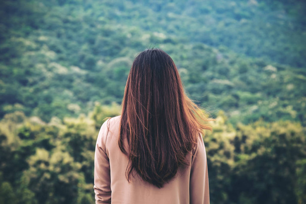 Una mujer se da la vuelta y se queda sola con la naturaleza verde y el fondo de montaña
 - Foto, Imagen