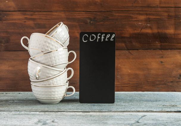 biały stosu kawy filiżanki i mała tablica na drewnianym blatem. W menu. Karta herbaty. Karta kawowa - Zdjęcie, obraz