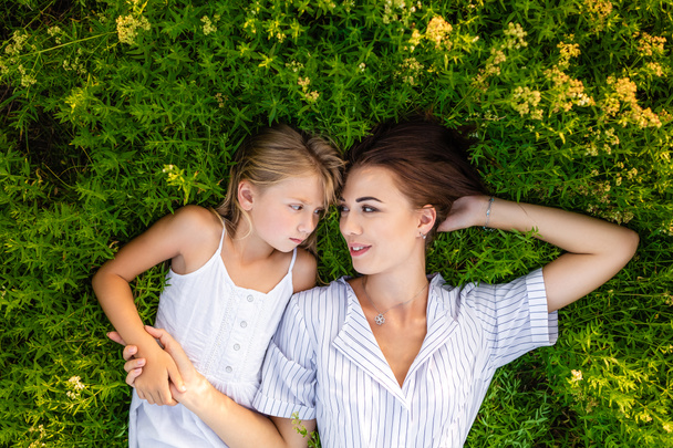 Widok z góry z matka i córka relaks podczas leżącego w kwieciste łąki i patrząc na siebie - Zdjęcie, obraz