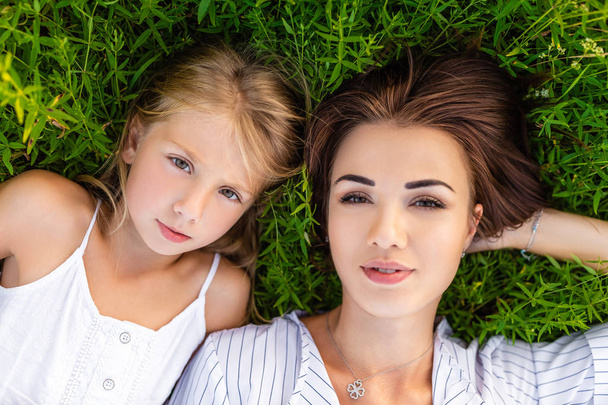 top view of mother and daughter lying on green grass and looking at camera - Valokuva, kuva