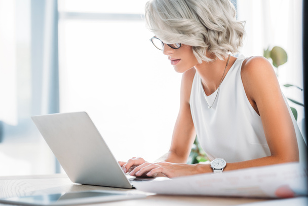 Zijaanzicht van prachtige zakenvrouw laptop gebruiken in office - Foto, afbeelding
