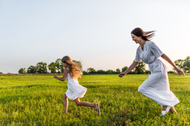 etkin anne ve kızı beyaz elbiseler yeşil çayır çalıştıran - Fotoğraf, Görsel