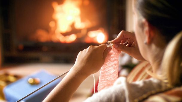 Image rapprochée d'une jeune femme assise au coin de la cheminée et tricotant un pull en laine
 - Photo, image