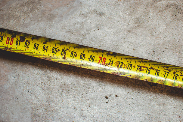 Крупный план старой ржаво-желтой измерительной ленты с черными цифрами, измеряющими сантиметры. Пункт, лежащий на пыльном полу склада
 - Фото, изображение