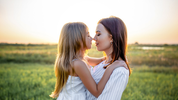portrait en gros plan de mère et fille embrassant et touchant le nez dans un champ vert au coucher du soleil
 - Photo, image