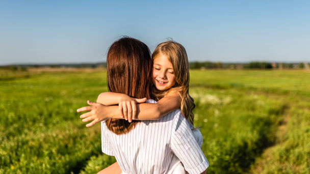 η μητέρα αγκαλιάζει με την κόρη της ευτυχισμένη στο πράσινο λιβάδι - Φωτογραφία, εικόνα